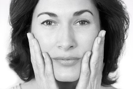 Middle-aged woman touching her cheeks with both hands.