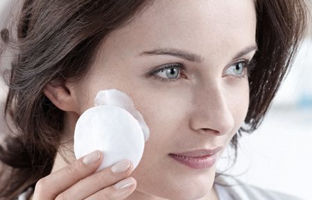 Woman applying cream with cotton pad on her face